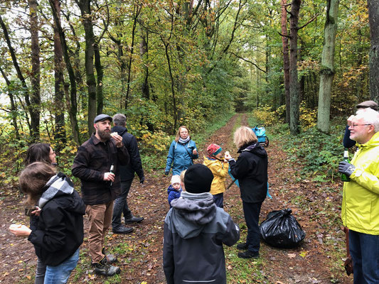Eine Gruppe von Menschen, darunter Kinder, steht auf einem Waldweg zusammen. Einige halten Getränke in der Hand und Müllsäcke liegen zugeknotet am Boden.